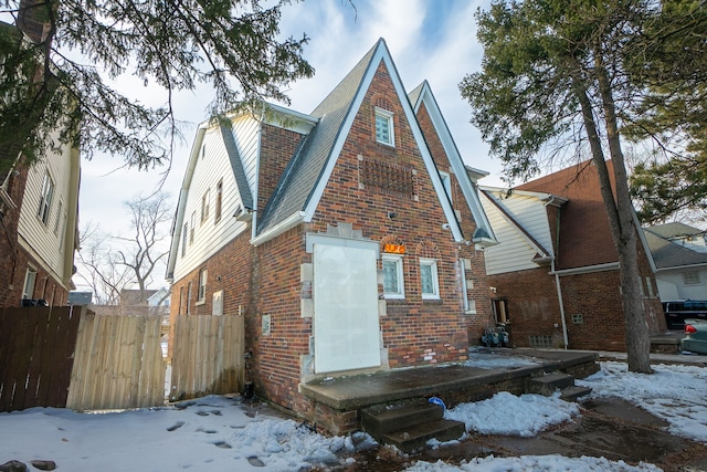 exterior space with brick siding, fence, and roof with shingles