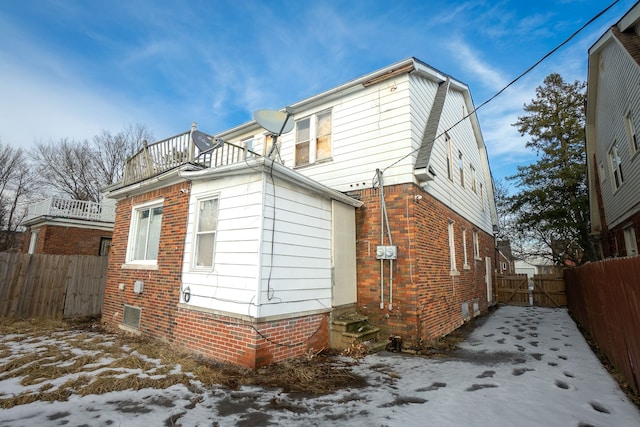 snow covered house with entry steps, brick siding, fence, and a balcony