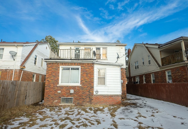 snow covered rear of property with a balcony, fence private yard, and brick siding