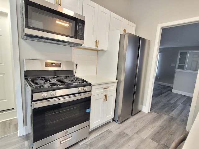 kitchen featuring light wood-style flooring, white cabinetry, light countertops, appliances with stainless steel finishes, and decorative backsplash