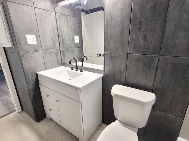 half bathroom featuring toilet, tile patterned floors, tile walls, and vanity