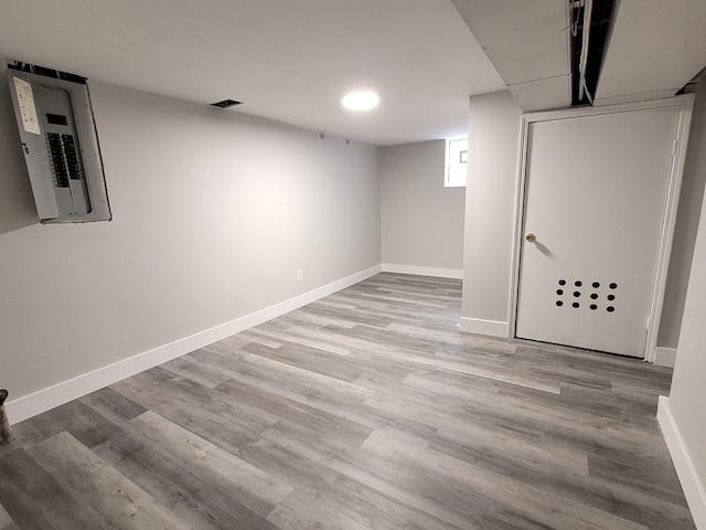 below grade area with baseboards, electric panel, and light wood finished floors