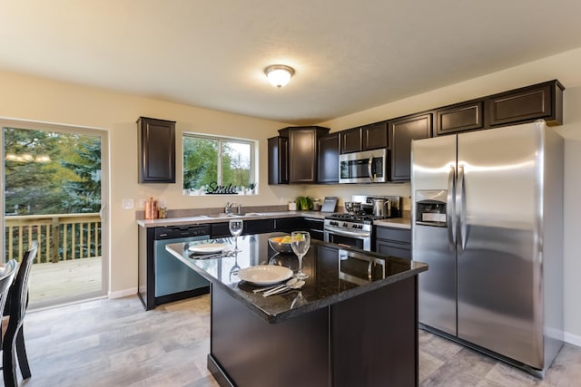 kitchen featuring dark brown cabinetry, dark stone counters, a kitchen island, stainless steel appliances, and a sink