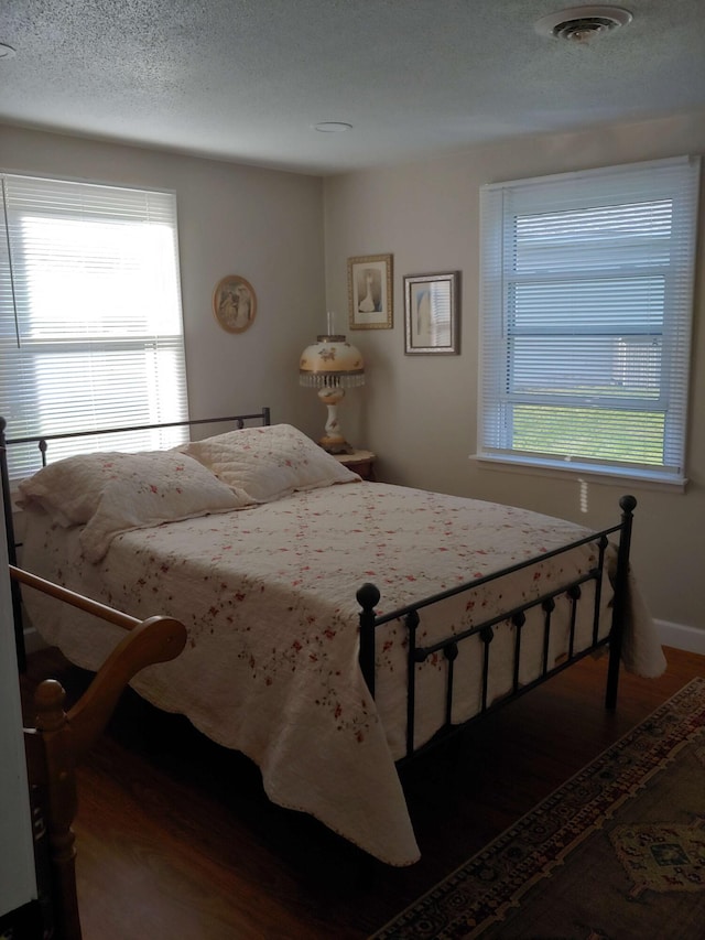 bedroom with visible vents, baseboards, a textured ceiling, and wood finished floors