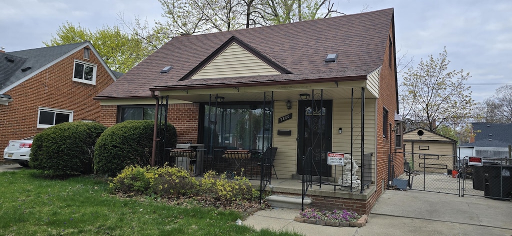 view of front facade featuring brick siding, a shingled roof, a gate, fence, and a front lawn