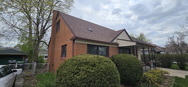 view of front of home with a shingled roof, brick siding, and fence