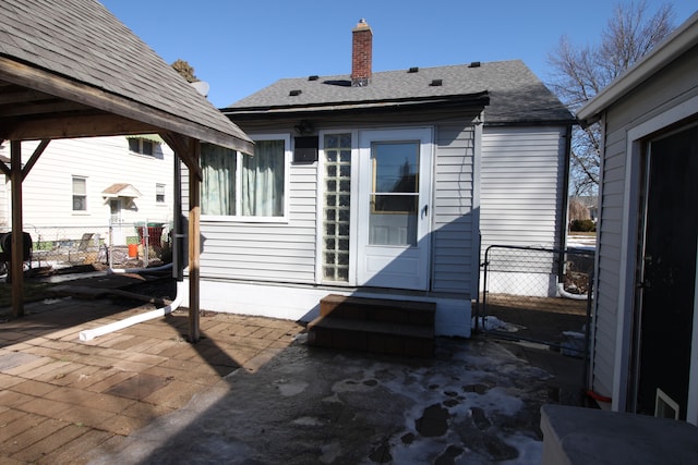 rear view of property featuring a shingled roof, a chimney, fence, and a patio