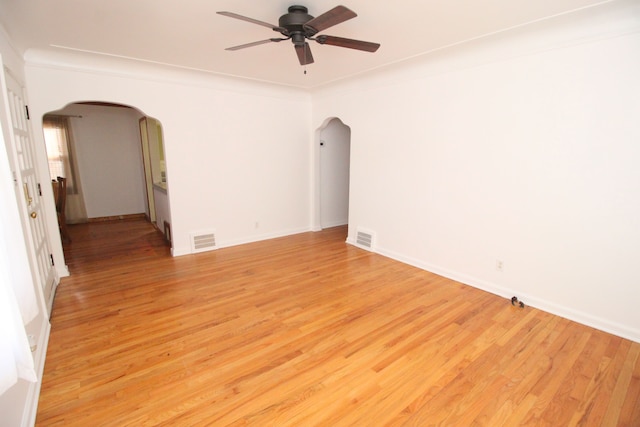 empty room with arched walkways, visible vents, and light wood finished floors