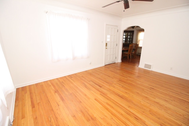 spare room featuring light wood-style flooring, visible vents, arched walkways, and baseboards