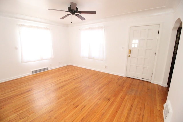 unfurnished room featuring light wood-type flooring, visible vents, arched walkways, and a wealth of natural light