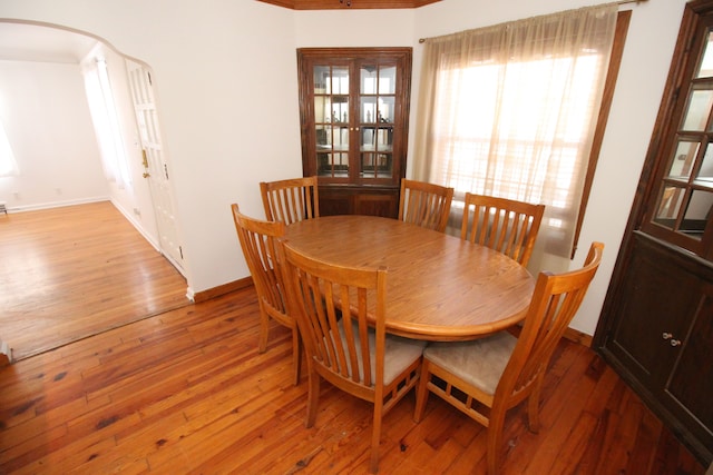 dining area with light wood-style flooring, arched walkways, and baseboards