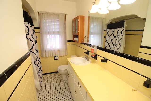 full bathroom featuring a wainscoted wall, tile walls, toilet, an inviting chandelier, and vanity