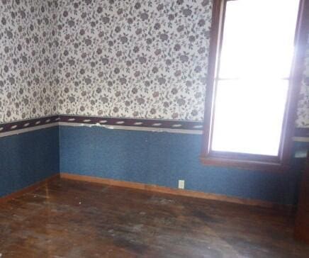 spare room featuring wallpapered walls, baseboards, and dark wood finished floors