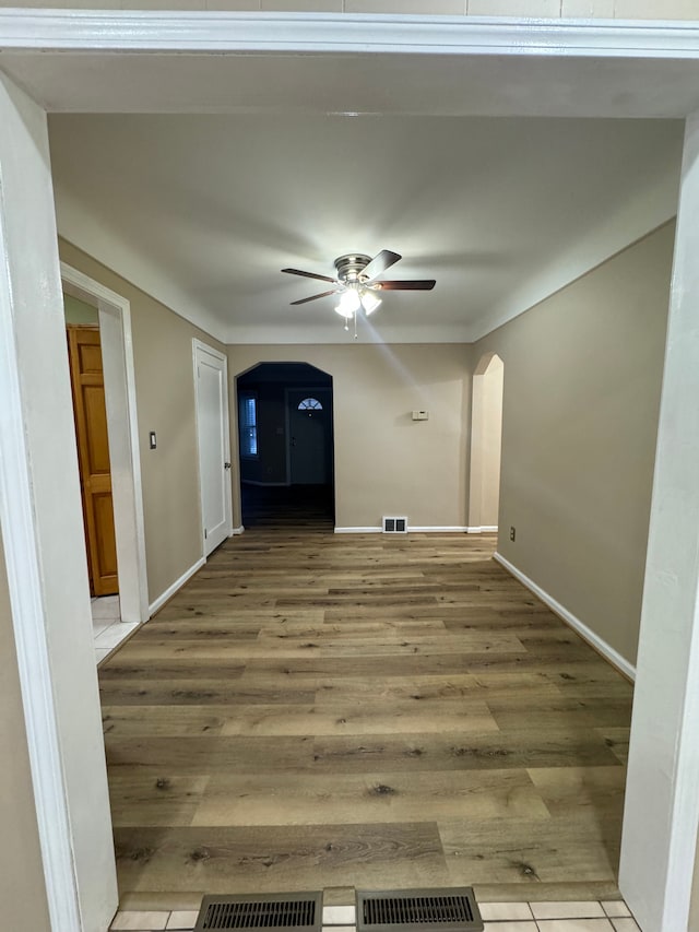 interior space featuring arched walkways, ceiling fan, light wood-style flooring, and visible vents