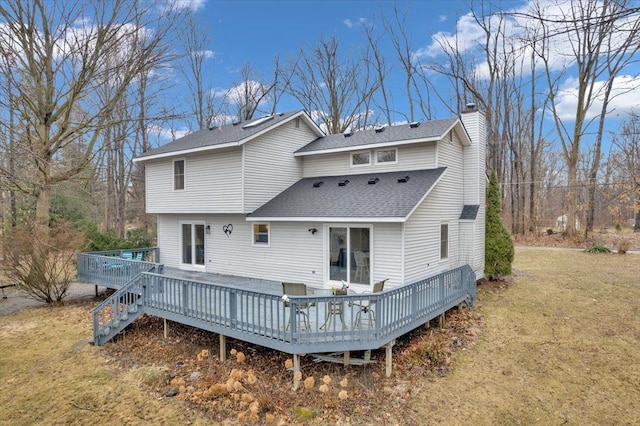 back of house with a deck, roof with shingles, a yard, and a chimney