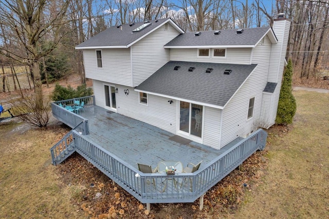 rear view of house featuring a wooden deck, a chimney, stairway, roof with shingles, and a yard