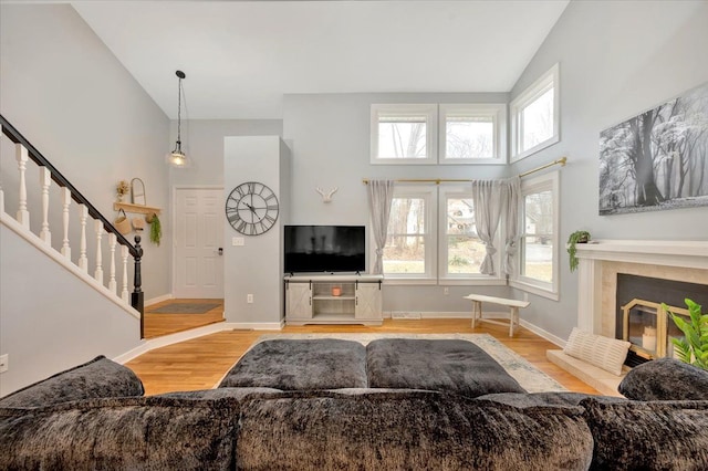 living area featuring stairs, a glass covered fireplace, wood finished floors, and a wealth of natural light