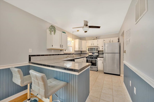 kitchen with a peninsula, visible vents, white cabinets, appliances with stainless steel finishes, and wainscoting