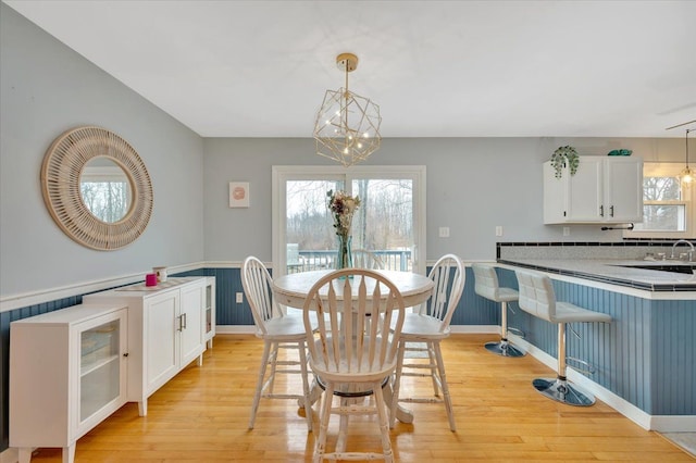 dining room featuring light wood-type flooring, an inviting chandelier, plenty of natural light, and wainscoting