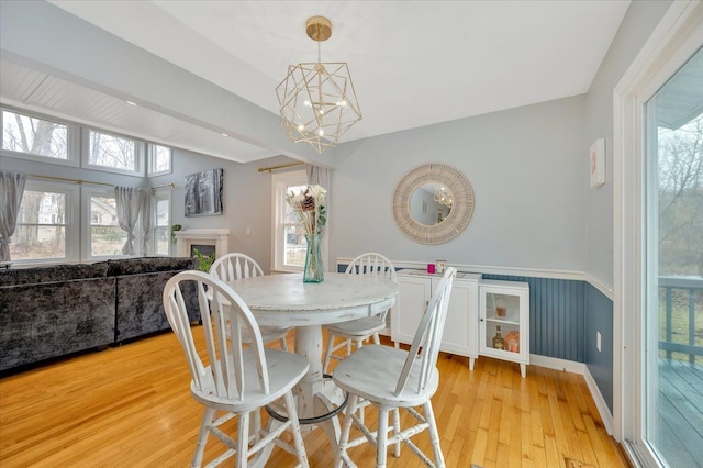 dining area featuring light wood-style floors, a wainscoted wall, vaulted ceiling, and an inviting chandelier