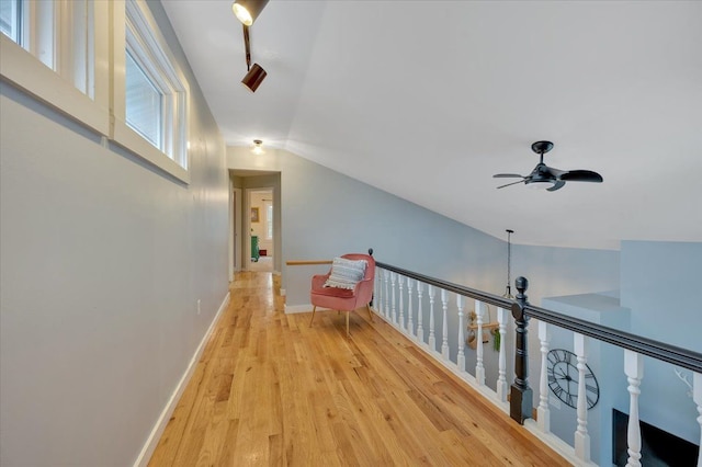 hall featuring light wood-style floors, baseboards, vaulted ceiling, and track lighting