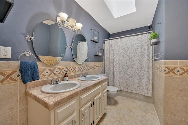 bathroom featuring a sink, a skylight, toilet, and tile walls