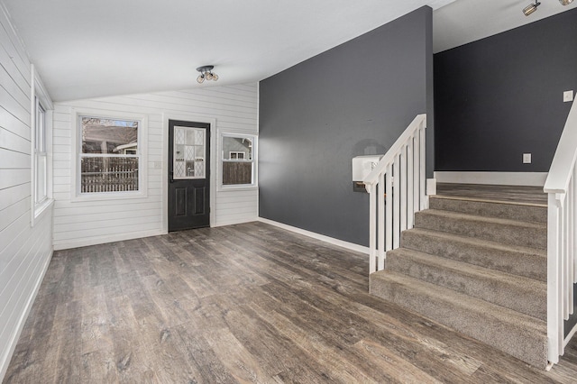 entrance foyer featuring dark wood-style floors, lofted ceiling, wood walls, baseboards, and stairs