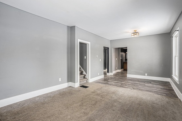 empty room featuring visible vents, dark carpet, stairway, and baseboards