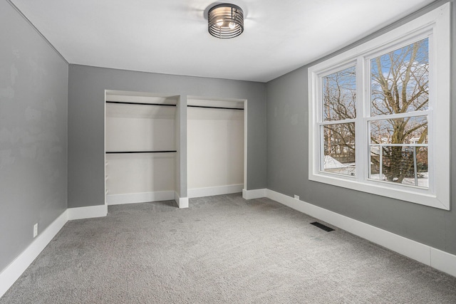 unfurnished bedroom with carpet floors, two closets, visible vents, and baseboards