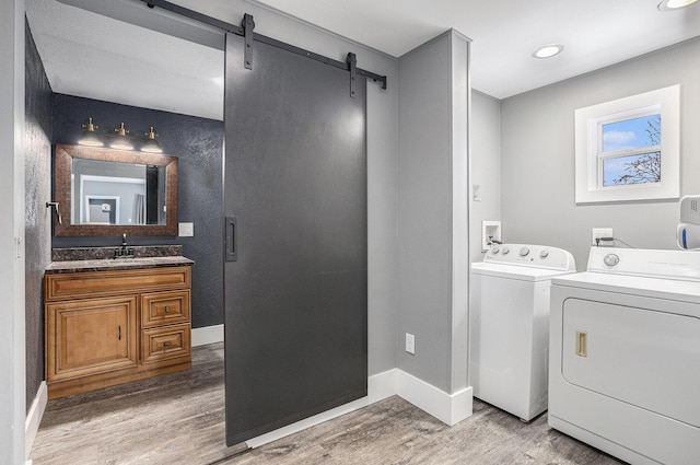 clothes washing area with wood finished floors, a sink, washer and clothes dryer, and a barn door