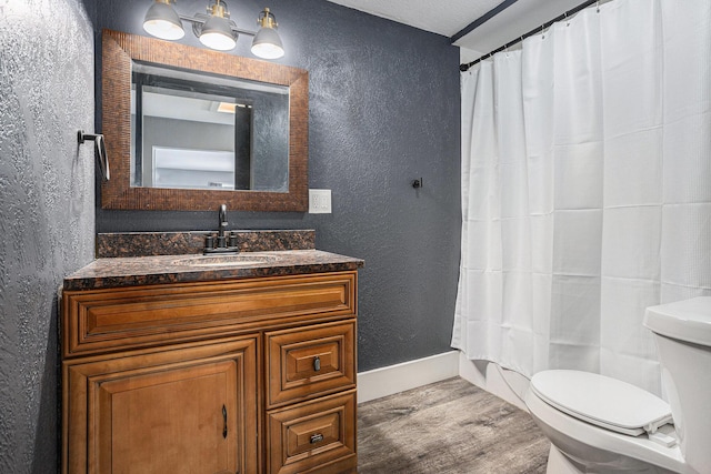 bathroom with toilet, vanity, wood finished floors, and a textured wall