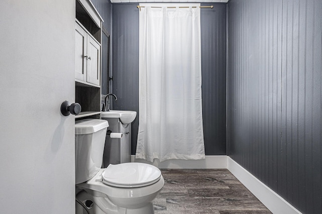 bathroom featuring toilet, shower / tub combo, a sink, wood finished floors, and baseboards