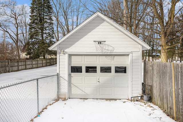 snow covered garage featuring a garage and fence