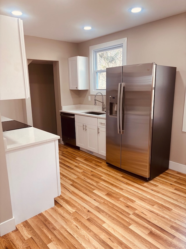 kitchen featuring stainless steel fridge, white cabinets, dishwashing machine, light wood-type flooring, and a sink