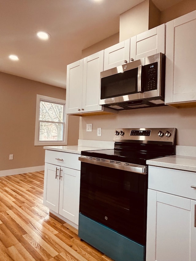 kitchen featuring light wood finished floors, baseboards, appliances with stainless steel finishes, light countertops, and white cabinetry