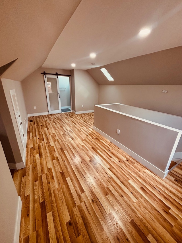 bonus room with light wood-style floors, a barn door, baseboards, and lofted ceiling with skylight