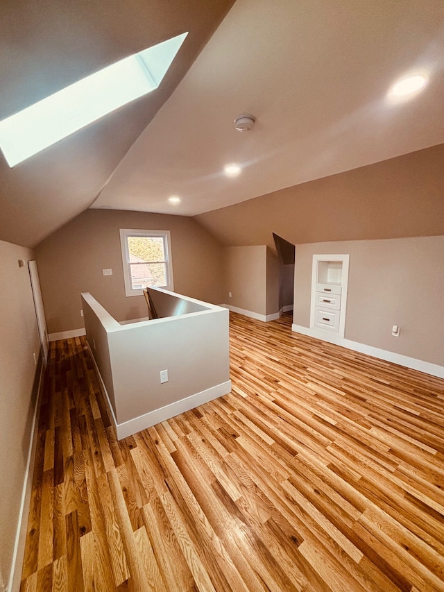 bonus room featuring vaulted ceiling with skylight, baseboards, and light wood finished floors