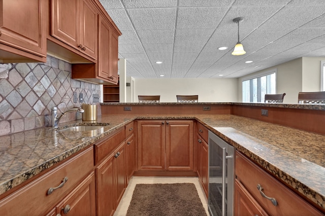 kitchen with decorative backsplash, brown cabinetry, a sink, dark stone countertops, and beverage cooler