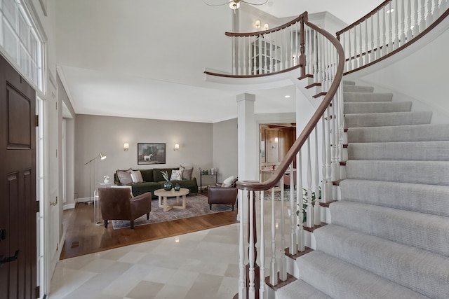 foyer entrance with stairway, light wood-style floors, a towering ceiling, and ornamental molding