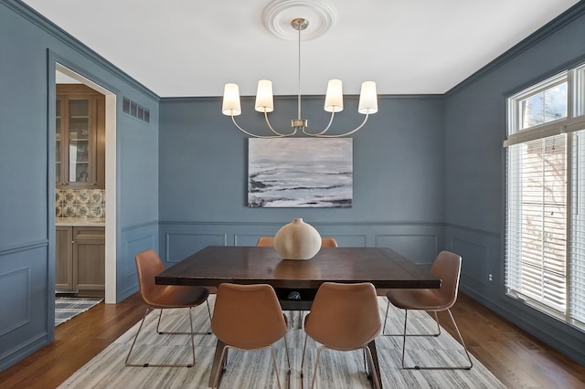 dining room with visible vents, a chandelier, crown molding, and wood finished floors