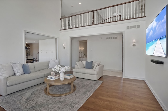 living area featuring a towering ceiling, baseboards, visible vents, and wood finished floors