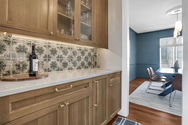 bar featuring a wainscoted wall, dark wood-type flooring, a sink, tasteful backsplash, and crown molding