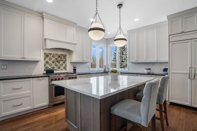 kitchen with a breakfast bar, a kitchen island, high quality appliances, dark wood finished floors, and custom range hood