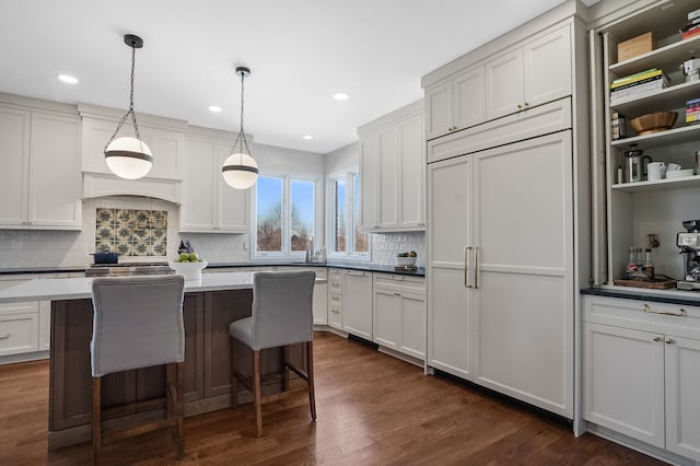 kitchen featuring a breakfast bar, a center island, dark wood finished floors, hanging light fixtures, and paneled refrigerator