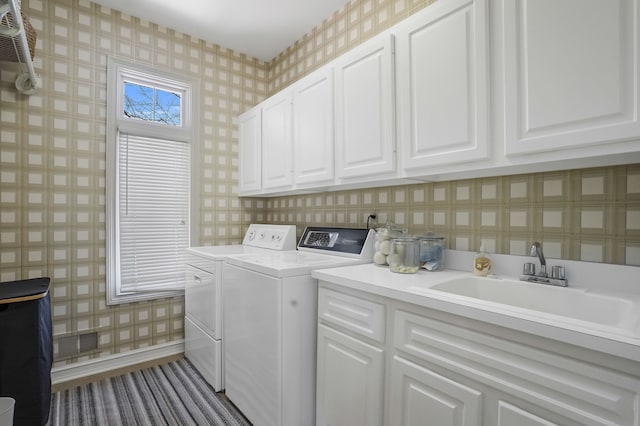 washroom with a sink, wallpapered walls, washer and clothes dryer, and cabinet space