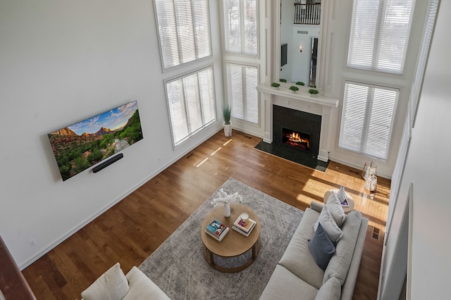 living area featuring a towering ceiling, a healthy amount of sunlight, a fireplace with flush hearth, and wood finished floors