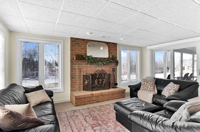 living room featuring carpet floors, a brick fireplace, a healthy amount of sunlight, and a drop ceiling