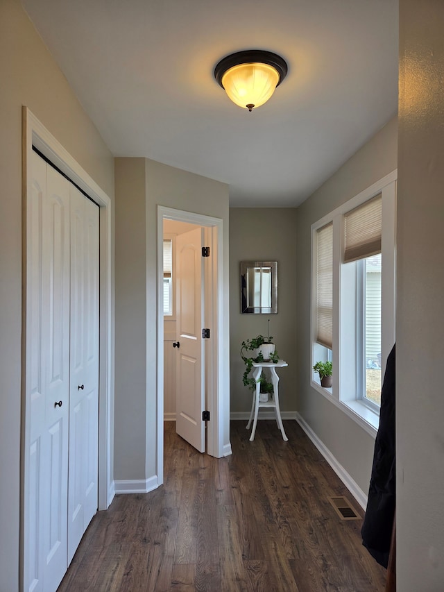 unfurnished bedroom with a closet, visible vents, dark wood-type flooring, and baseboards