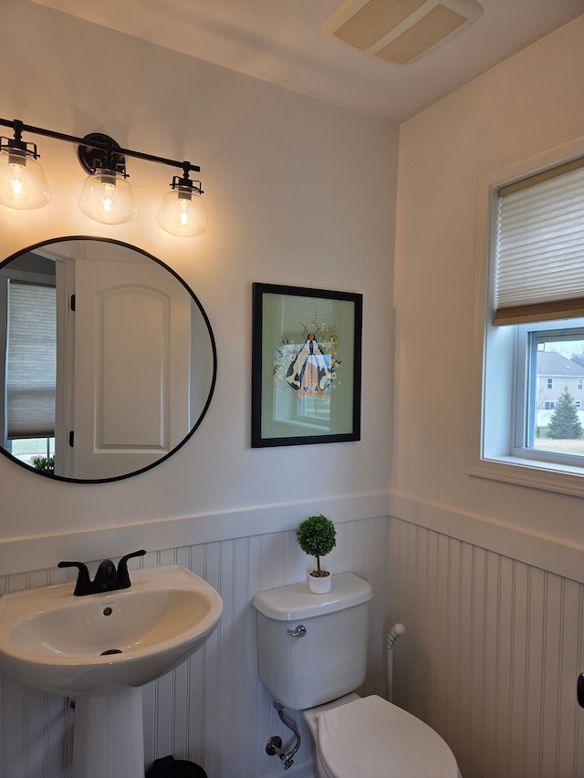 half bathroom with a wainscoted wall, toilet, visible vents, and a sink