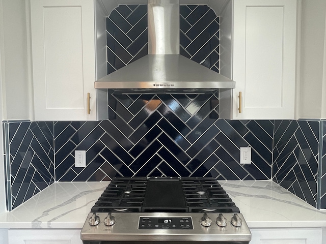 kitchen with light stone counters, white cabinetry, stainless steel gas range oven, and wall chimney exhaust hood